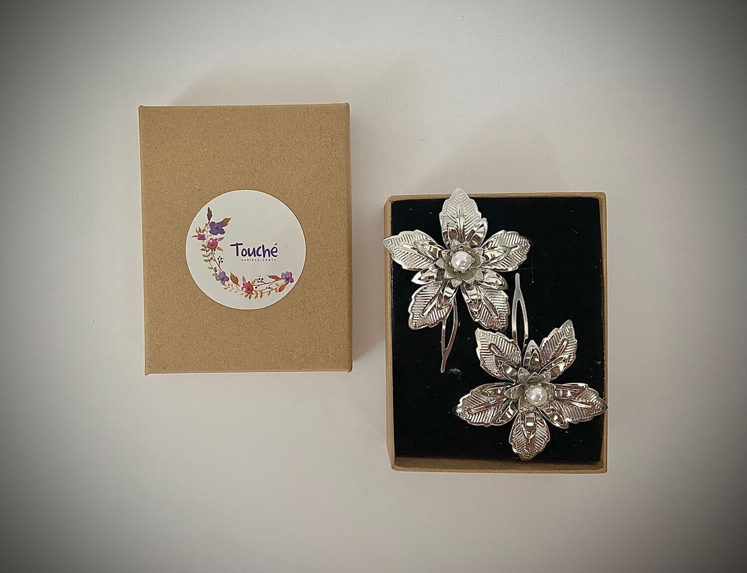 Conjunto compuesto por 2 horquillas de flores de unos 5 cm de diámetro con perla central.

Se pueden adquirir unos pendientes desmontables a conjunto (puede usarse sólo la perla o todo el pendiente unido).