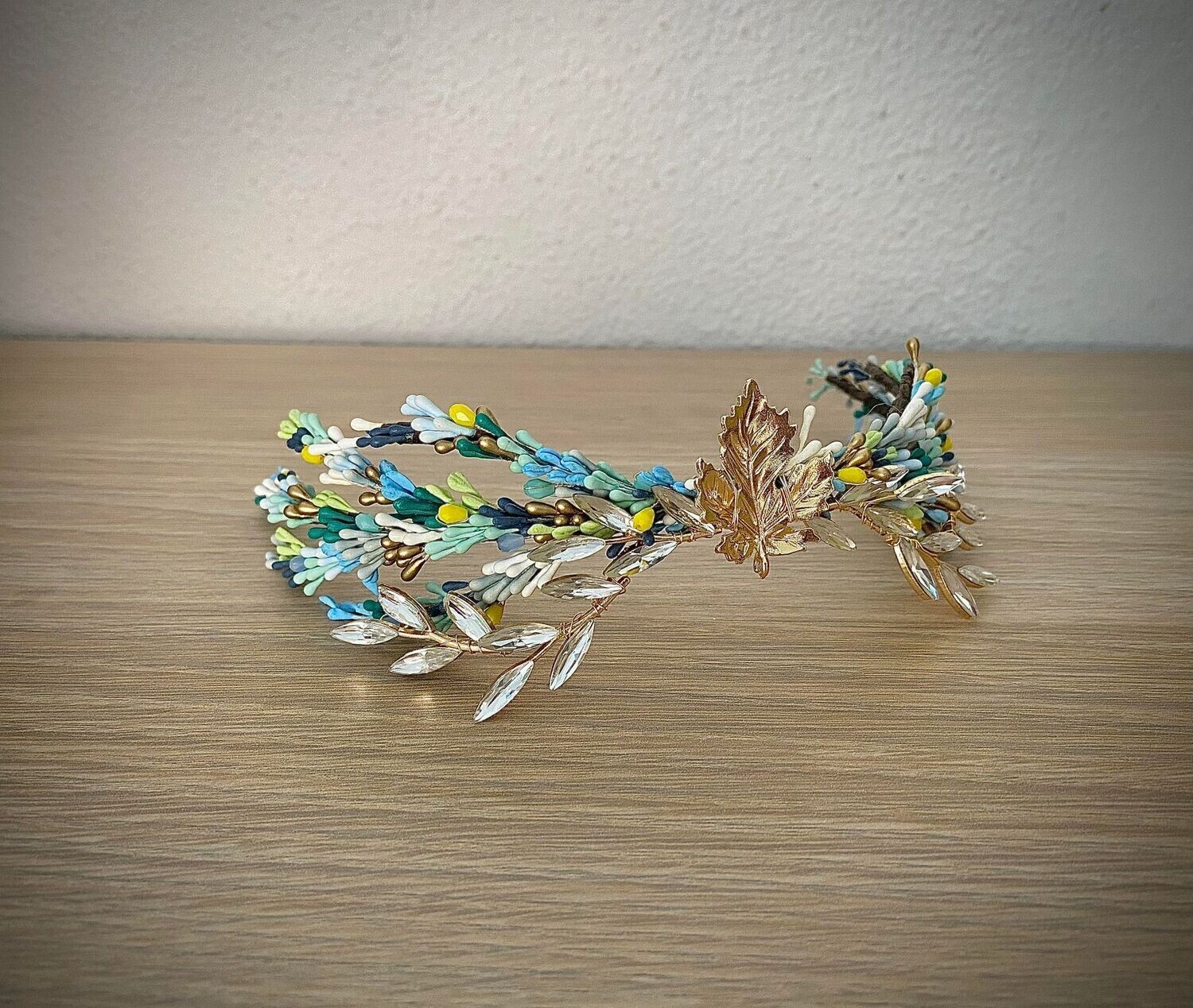 Tocado de unos 26 cm de longitud compuesto por pistilos en tonos azules y verdes con hoja dorada central y ramas en cristal transparente. Se puede desmontar y conseguir 3 piezas separadas.
