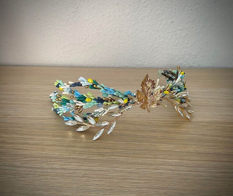 Tocado de unos 26 cm de longitud compuesto por pistilos en tonos azules y verdes con hoja dorada central y ramas en cristal transparente. Se puede desmontar y conseguir 3 piezas separadas.