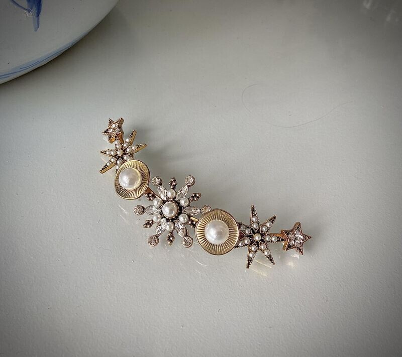 Tocado de metal de unos 11 cm de longitud en base dorada formado por estrellas con cristales transparentes y perlas.