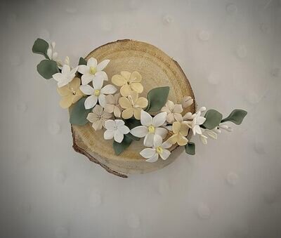 Tocado de porcelana de unos 20 cm de longitud compuesto por flores blancas y amarillas pálidas y hojas verdes.