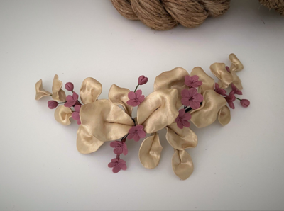 Tocado de porcelana de unos 24 cm de longitud con hojas de eucalipto en tono champagne y pequeñas flores en rosa fuerte.