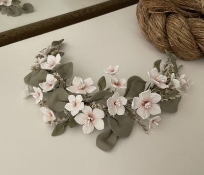 Tocado de porcelana y flores preservadas de unos 30 cm de longitud formado por hojas verdes y flores blancas con el centro rosa.