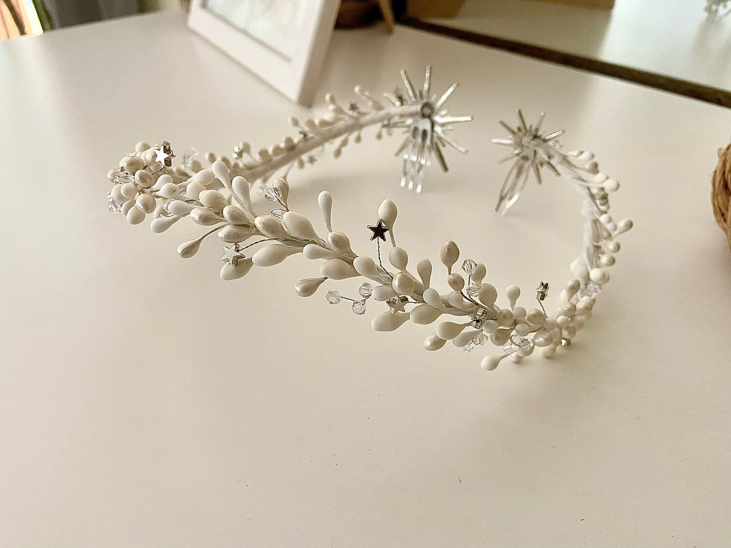 Corona de novia de pistilos blancos y nacarados con cristales transparentes y pequeñas estrellas terminada con 2 estrellas grandes e irregulares en la parte trasera.

El color de las estrellas puede ser dorado o plateado. Puedes incluir pistilos de otro color si quieres que conjunte con tus complementos.