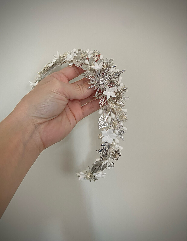 Tiara joya de novia compuesta por diferentes detalles dentro de los que destacan las flores, las hojas y los pistilos con una estrella central. Se caracteriza por ser una tiara con acabado en pico en el centro y por tener piezas de metal y de porcelana.

Queda preciosa si la combinas con horquillas en la parte trasera de la cabeza ya que se conseguimos equilibrar el look aportando luminosidad en la zona posterior.

Su peculiaridad es que puede utilizarse también como tocado trasero por su tamaño, consiguiendo con una misma pieza lucir dos looks.

No dudes en preguntar por personalizaciones para esta pieza.