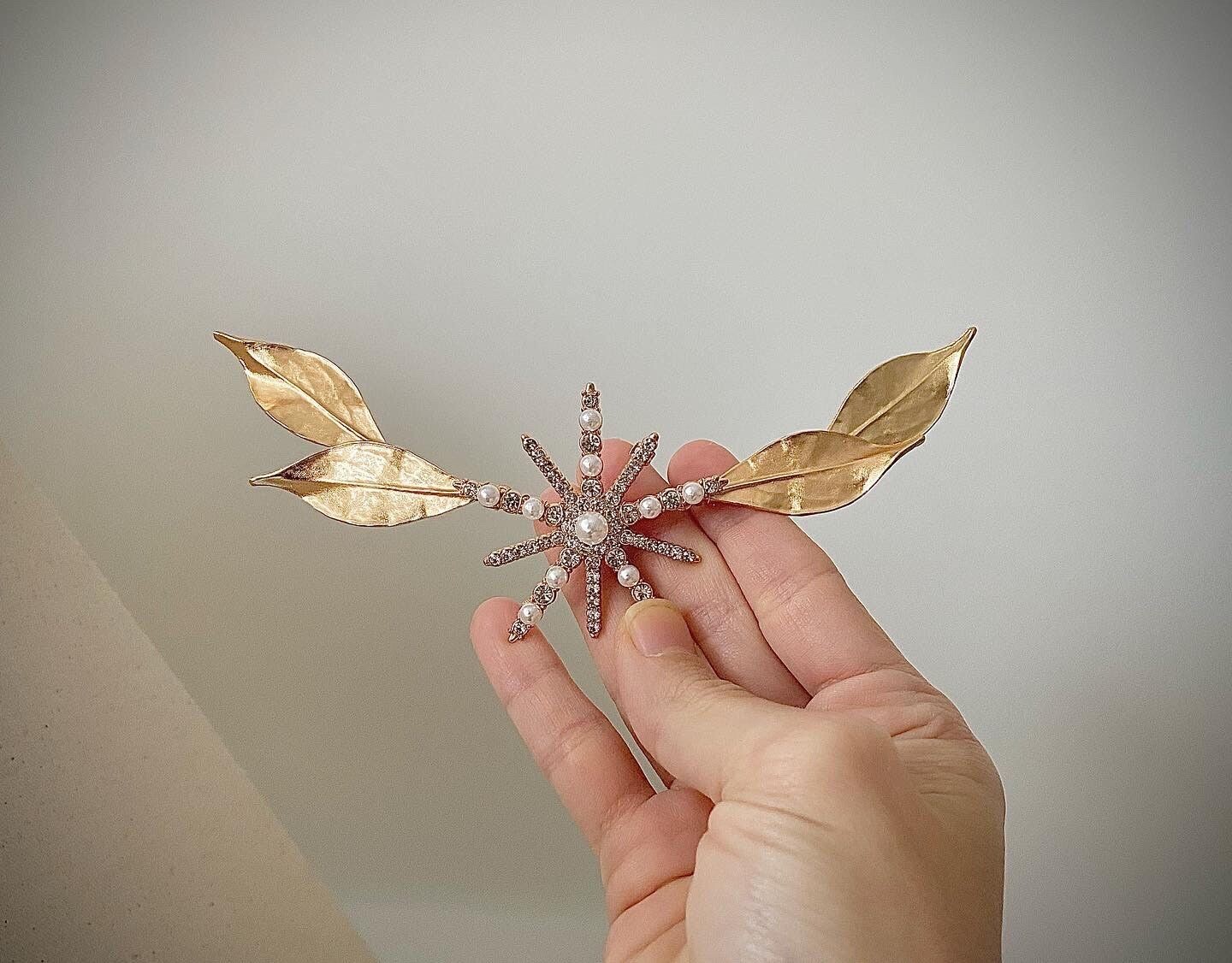 Tocado de novia con Estrella Central La Boheme Tocado de unos 14 cm de longitud compuesto por 4 hojas en tono dorado brillante y una estrella dorada con perlas y cristales transparentes situada en la parte central.
Se puede confeccionar también con las hojas en plata brillante y estrella en base plata.