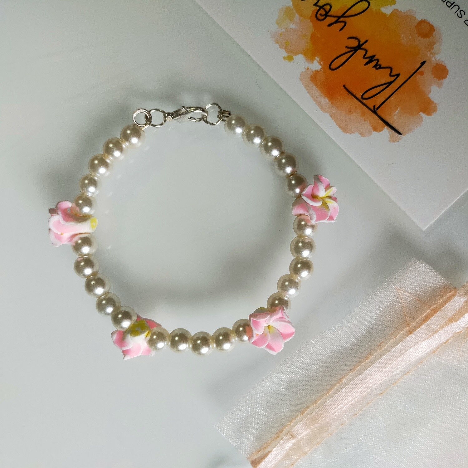 Armband mit weißer Perlen und vier Blumen in verschiedenen Farben 