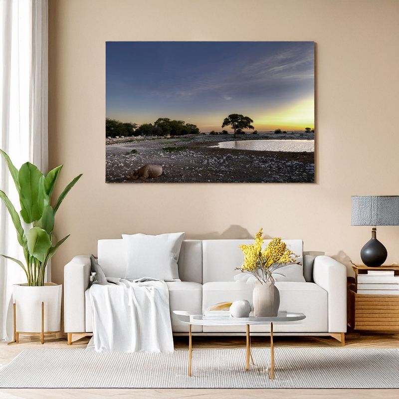 Etosha National Park - Evening Visitors Framed photo of a resting rhino at sunset near a waterhole, under a wide blue sky and golden horizon.