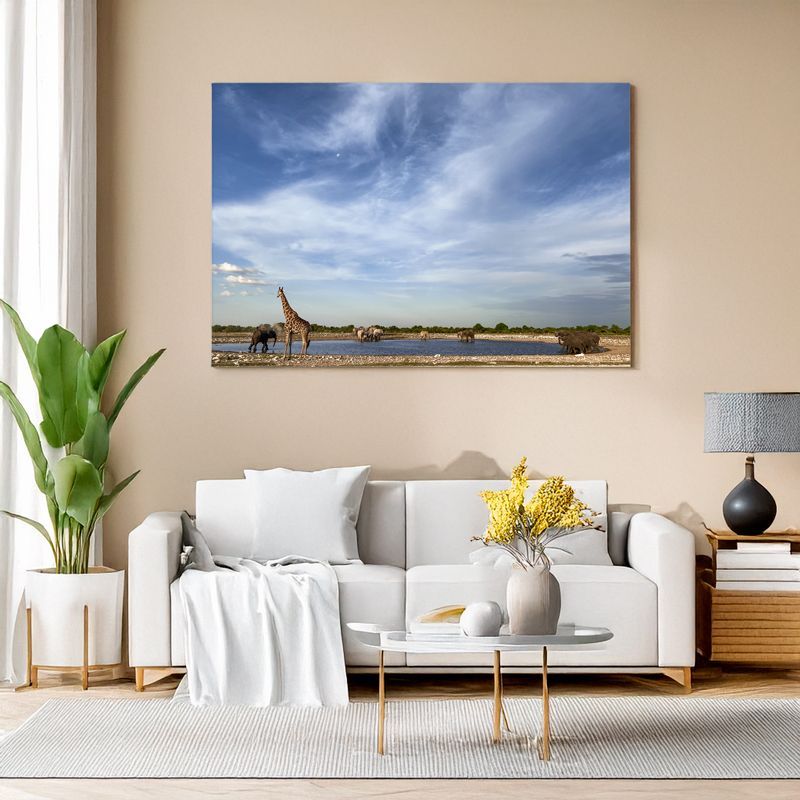 Modern living room with white sofa, canvas of giraffe and wildlife at a waterhole under a wide sky.