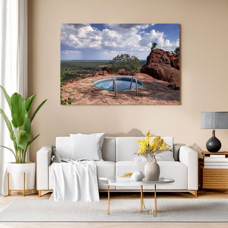 Modern living room with white sofa, canvas of a circular pool on a rocky terrace with vast scenic view.