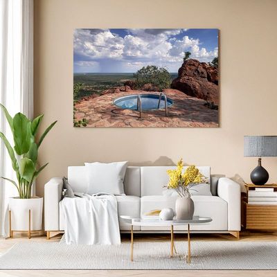 Modern living room with white sofa, canvas of a circular pool on a rocky terrace with vast scenic view.