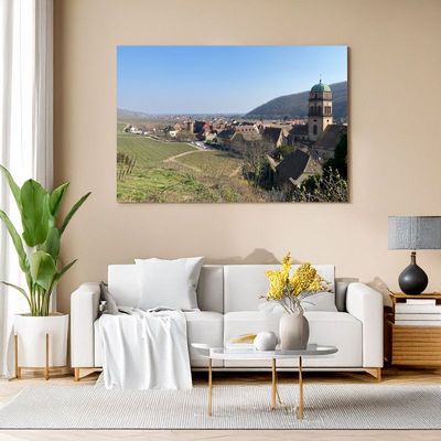 Wohnzimmer mit Leinwandbild eines Dorfes inmitten von Weinbergen.