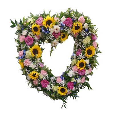 Couronne funéraire en cœur avec tournesols, roses roses, œillets, delphinium et verdure sur chevalet en bois