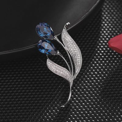 Close-up of blue and silver tulip flower brooch with cubic zirconia on dark textured background
