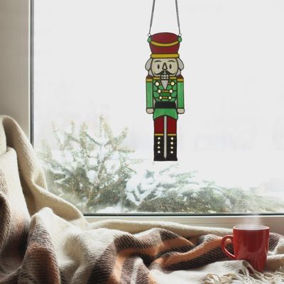 Nutcracker stained glass window panel hanging in window catching sunlight
