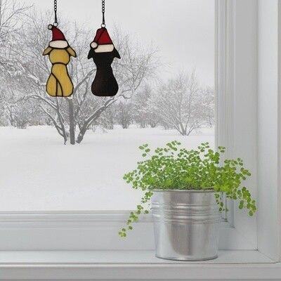Chiots en verre Tiffany blanc et noir avec chapeaux suspendus à la fenêtre enneigée
