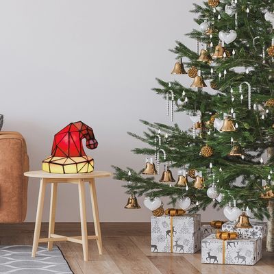 Santa hat stained glass Tiffany lamp on stool beside decorated Christmas tree
