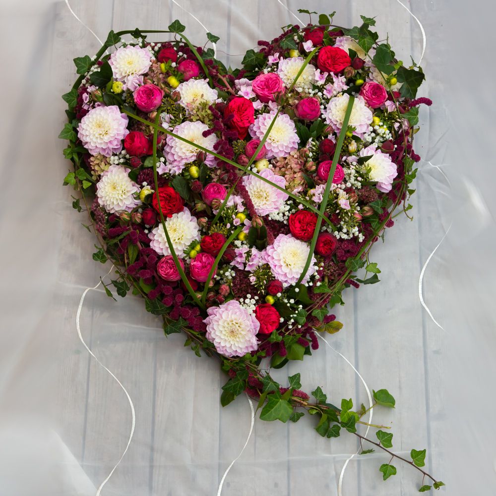 Composition de deuil en forme de cœur avec des fleurs roses, fuchsia et vertes sur une table