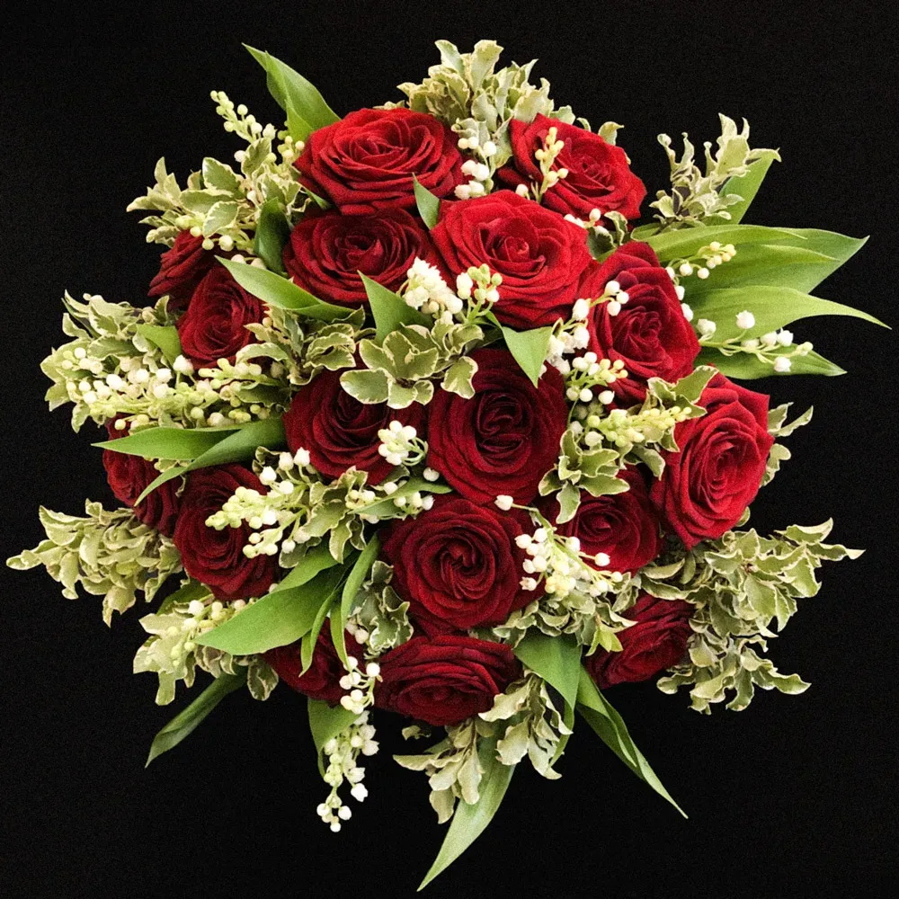 Vue du dessus d'un bouquet de roses rouges, muguet et feuillage décoratif sur fond sombre.