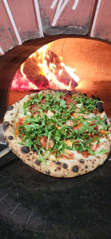 Neapolitan style pizza with Calabrese Salami and Arugula held in front of a wood fired oven 