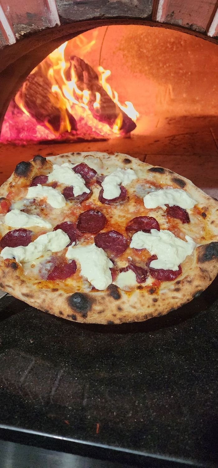 Neapolitan style pizza with Wagyu beef salami and burrata cheese held in front of a wood fired oven 