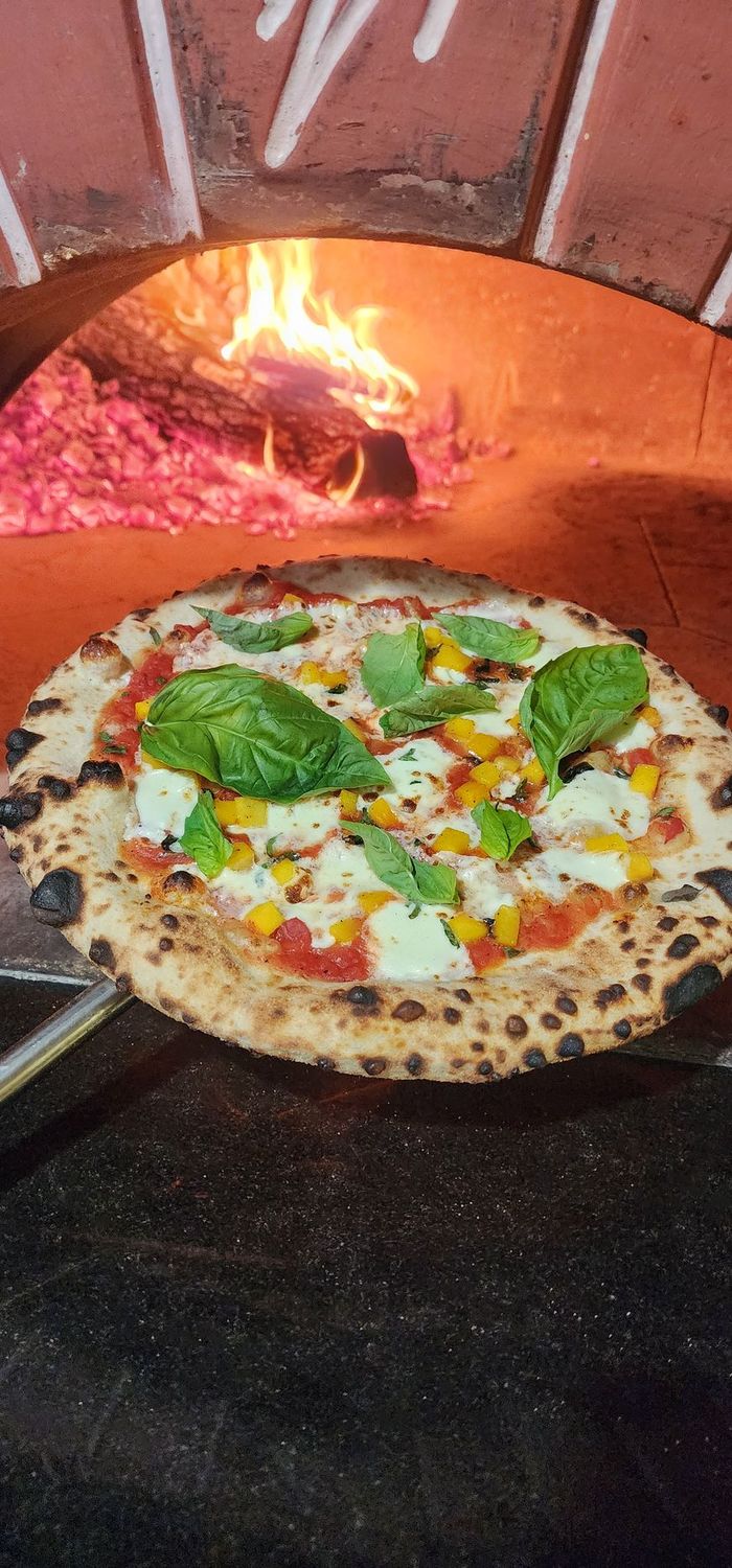 Neapolitan style pizza with butternut squash, basil, fresh mozzarella, san marzano tomato sauce, fresh oregano and caramelized butter held in front of a wood burning oven