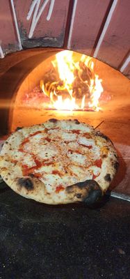 Neapolitan style pizza with san marzano tomato sauce and fresh mozzarella held in front of a wood fired oven