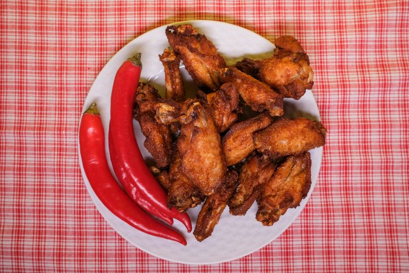 A plate with chicken wings and red peppers on a table 