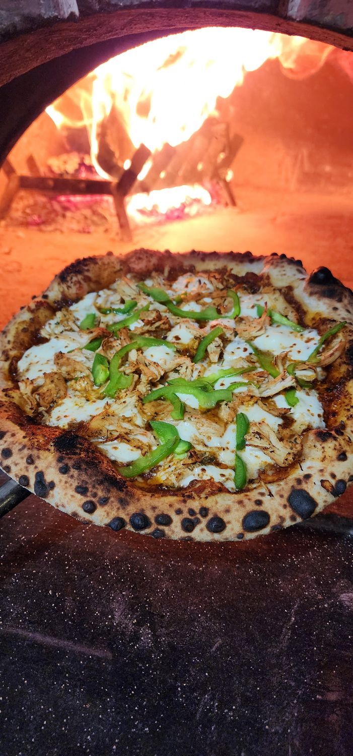 Neapolitan Style Pizza with Chicken, Peppers and chipotle sauce held in front of a wood fired oven