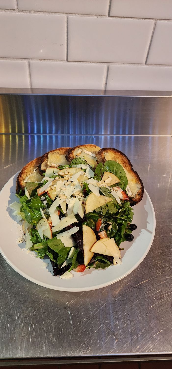 Salad topped with fruits and cheese on a stainless steel table with white tile background