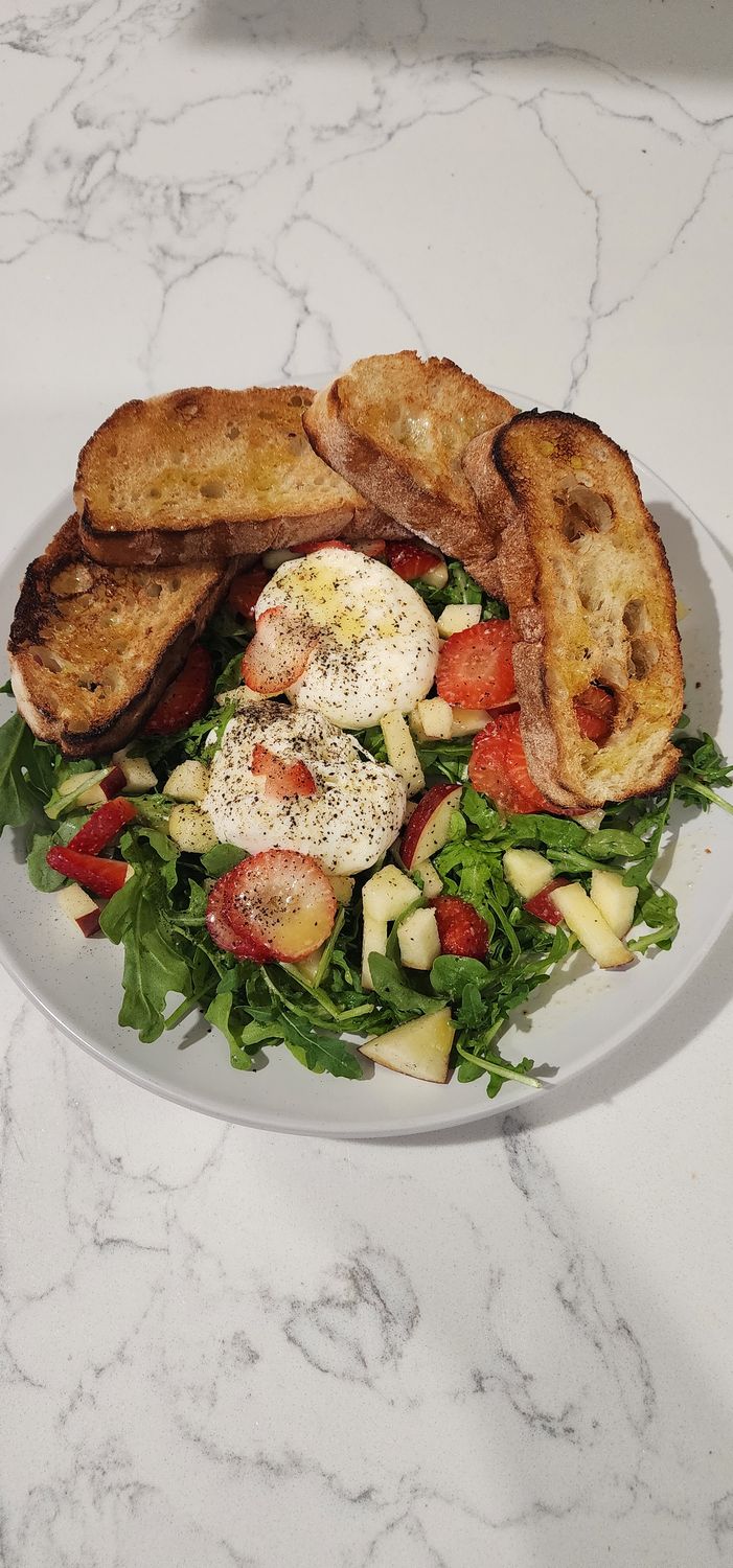 Salad plate with Arugula, Strawberries, fruits, Burrata Cheese and bread on a white marble counter top. 