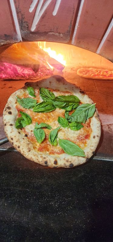 Margherita Neapolitan style pizza with san marzano sauce and house made mozzarella and basil held in front of a wood fired oven