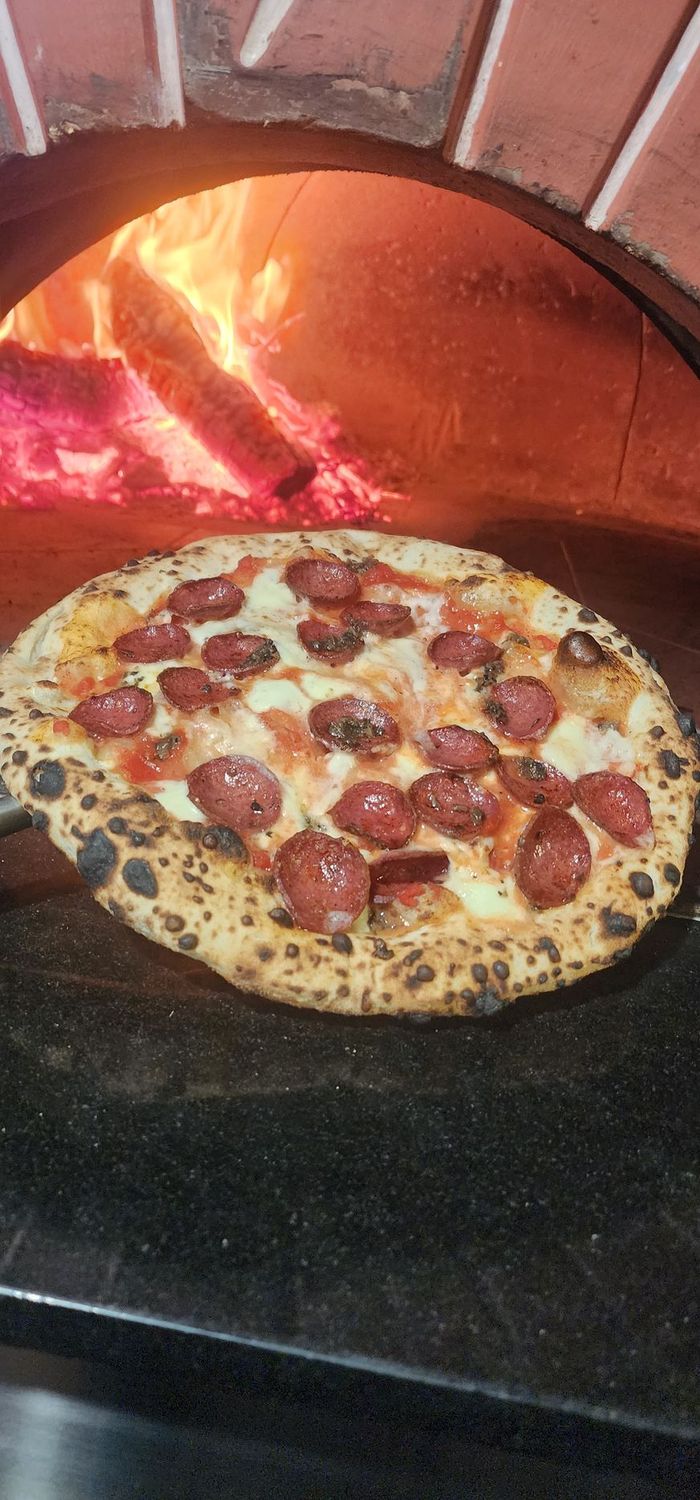 Tartufo e Agnello Neapolitan style pizza with lamb salami and black truffle held in front of a wood fired oven