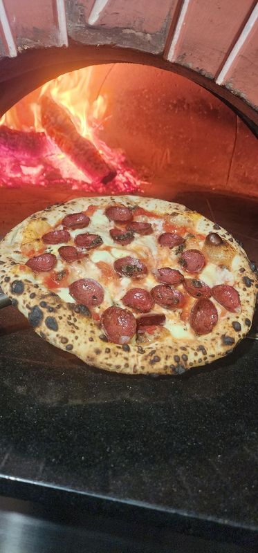 Tartufo e Agnello Neapolitan style pizza with lamb salami and black truffle held in front of a wood fired oven