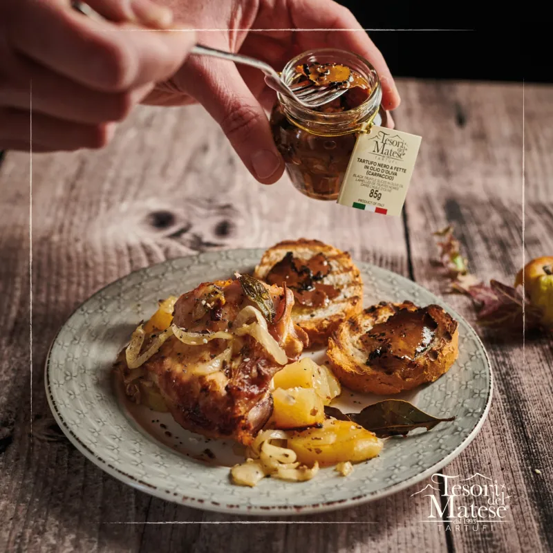 pair of hands scooping truffles out of a jar to add to a plate of food on a wooden table top