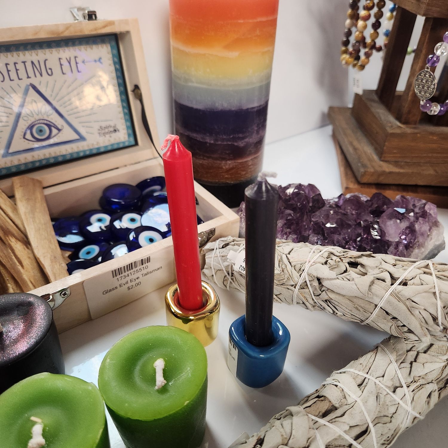 Chime Candles (single) Red and black chime candles in gold and blue holders on a cluttered witchy display with candles, incense, and crystals.