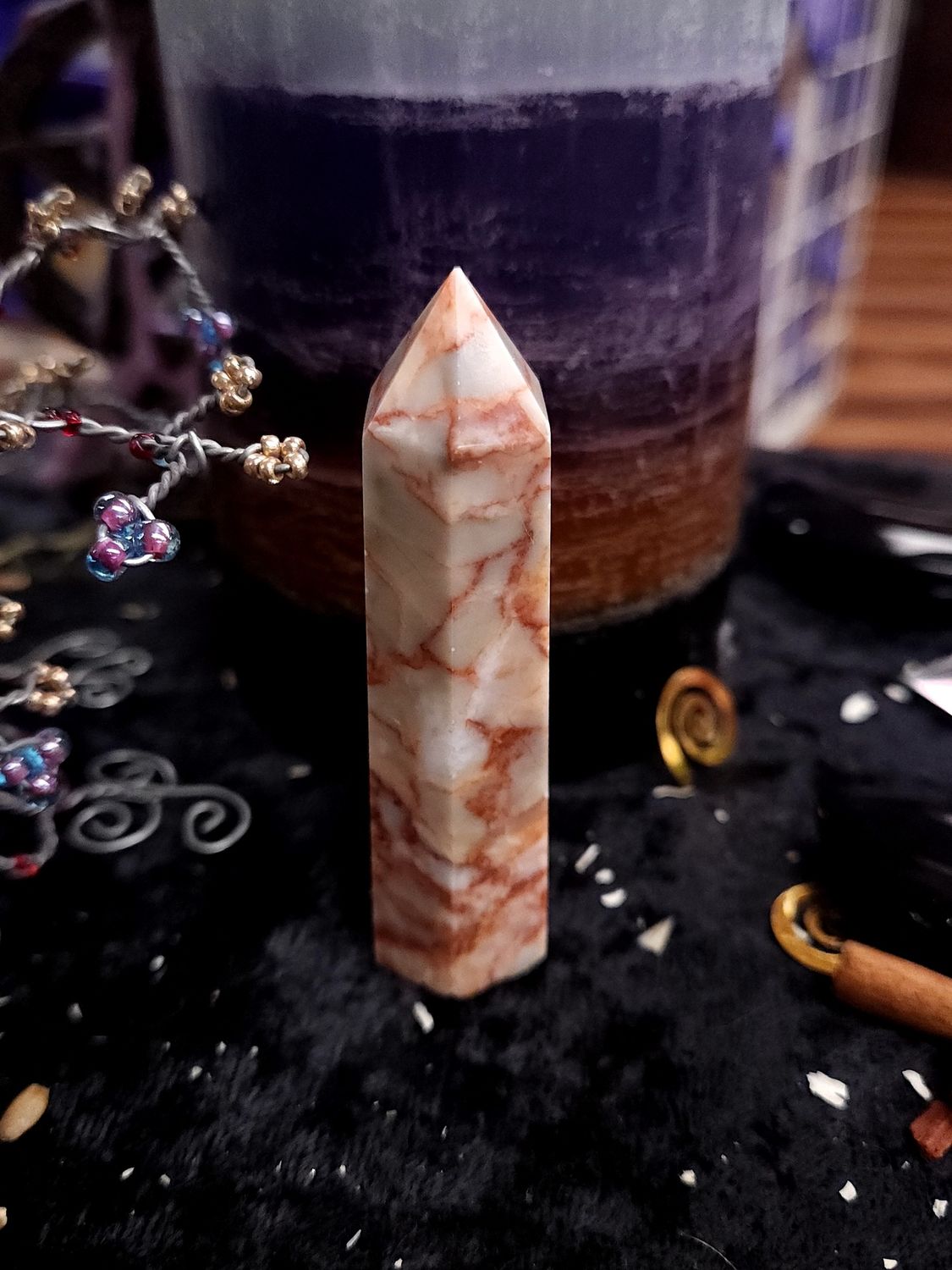 Red Vein Jasper Tower 70mm Creamy white 77mm red vein jasper tower with orange-red veining on a black altar cloth before a purple layered candle.