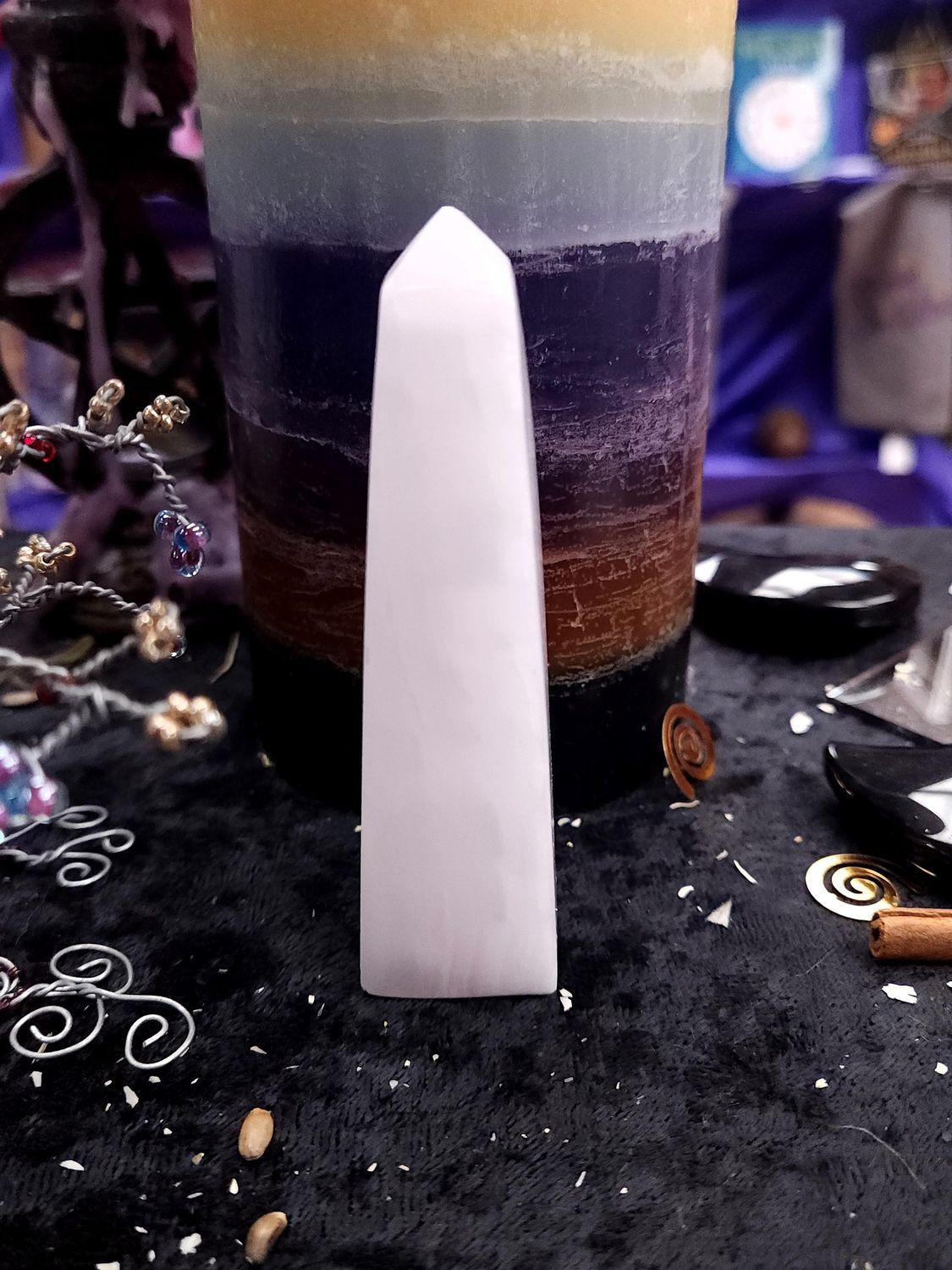 Tall 95mm pale pink calcite tower with a slim profile on a black altar cloth before a layered rainbow candle.