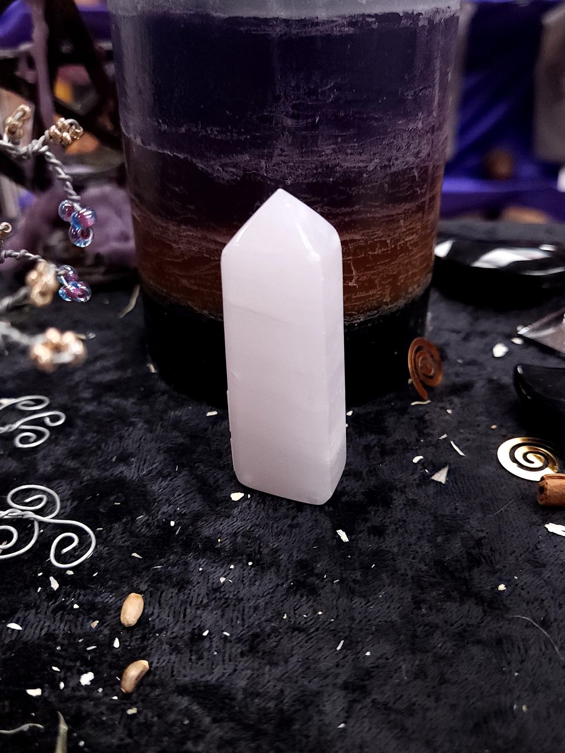 Short 64mm pink calcite tower on a black altar cloth in front of a layered purple candle.