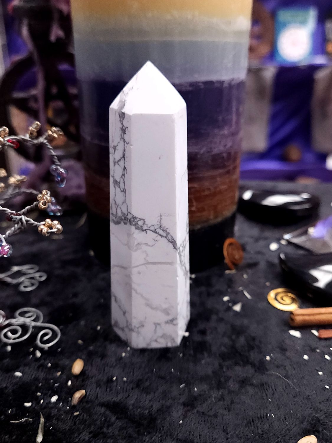 Tall 97mm white howlite tower with fine gray veining on a black altar cloth before a rainbow pillar candle.