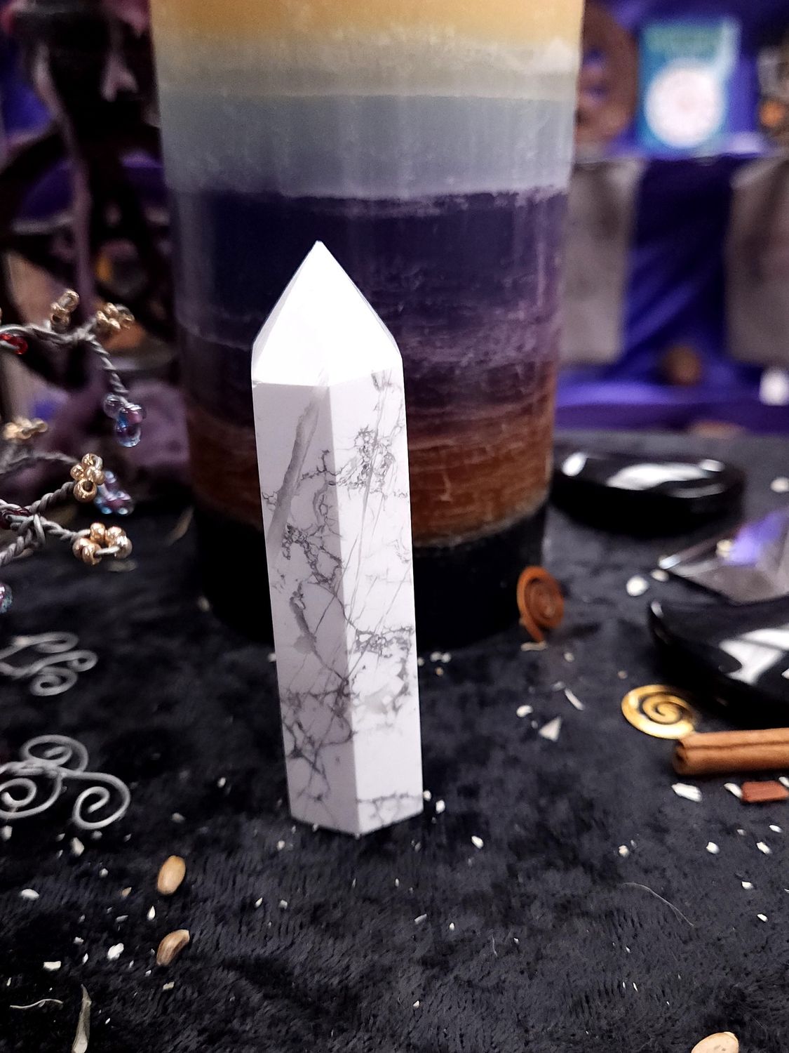 Still Waters Howlite Tower 86mm Slim 86mm white howlite tower with gray veining on a black altar cloth before a rainbow pillar candle.