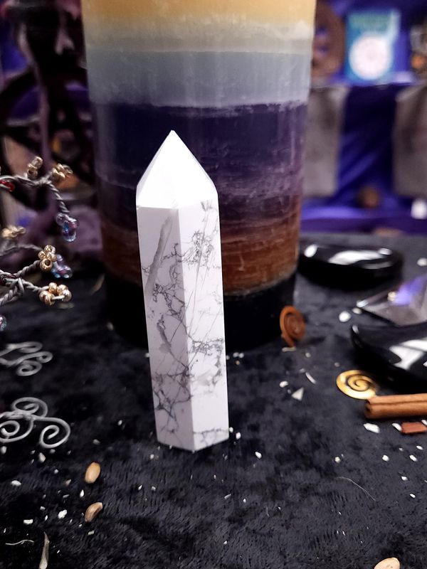 Still Waters Howlite Tower 86mm Slim 86mm white howlite tower with gray veining on a black altar cloth before a rainbow pillar candle.