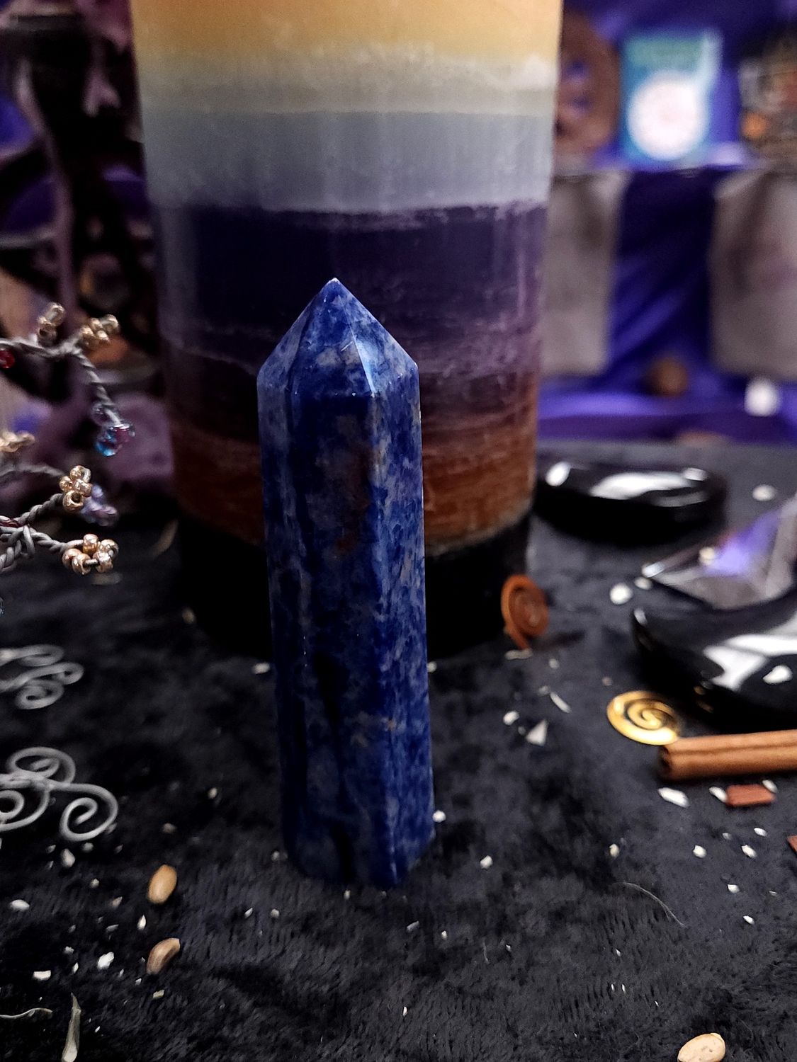 Truthspeaker Sodalite Tower 85mm Tall 85mm deep blue sodalite tower on a black altar cloth in front of a rainbow pillar candle.