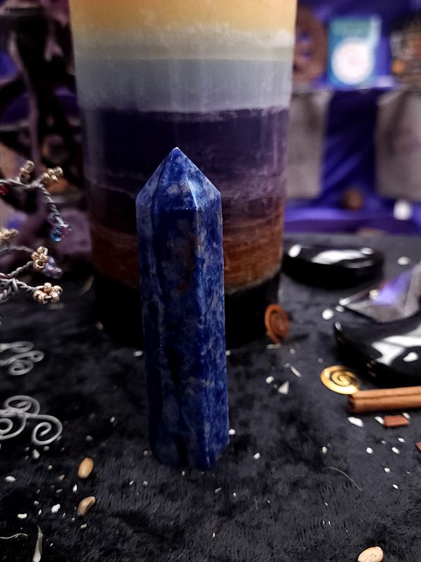 Truthspeaker Sodalite Tower 85mm Tall 85mm deep blue sodalite tower on a black altar cloth in front of a rainbow pillar candle.