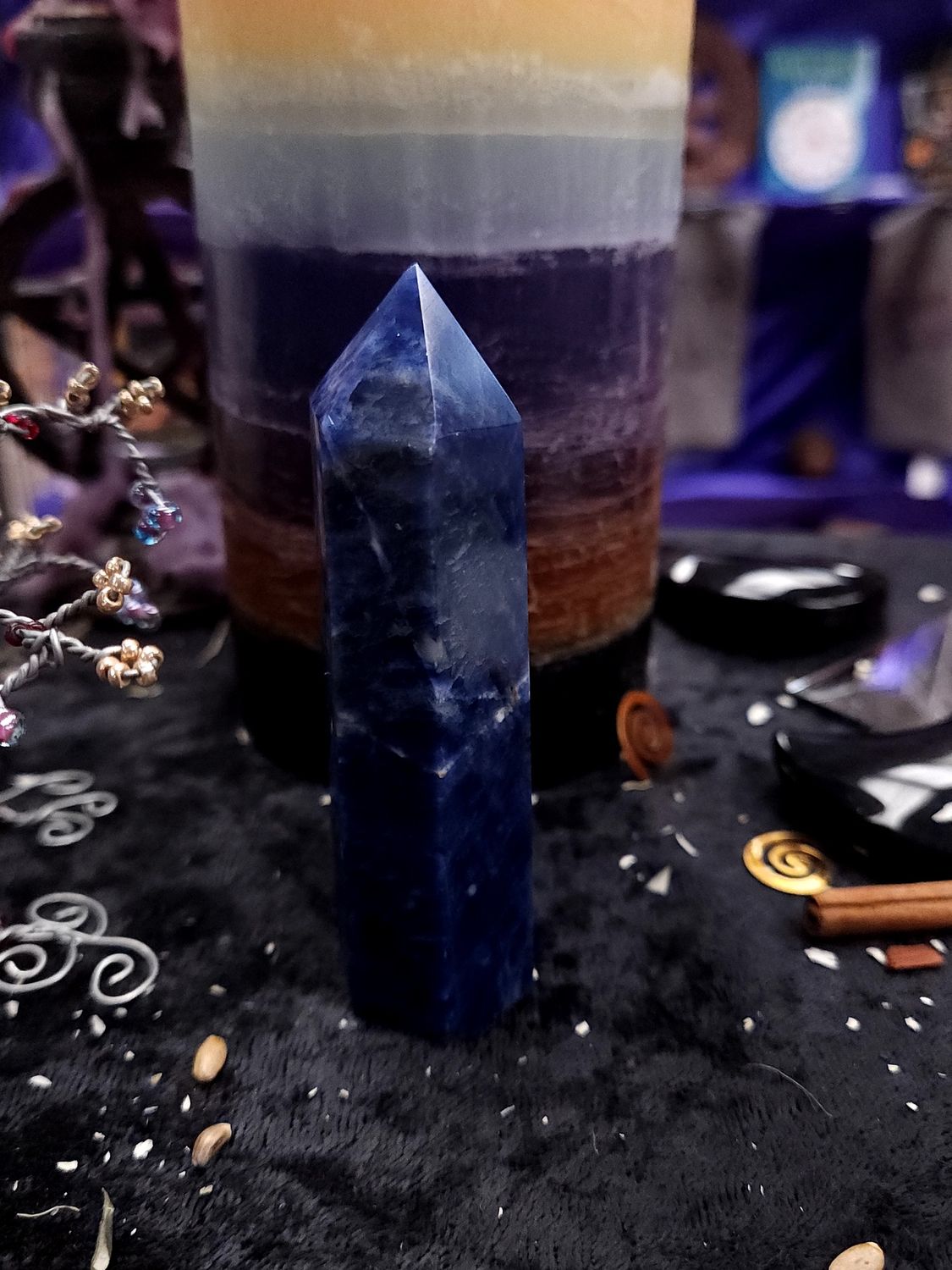 Tall 91mm deep blue sodalite tower on a black altar cloth in front of a rainbow pillar candle.
