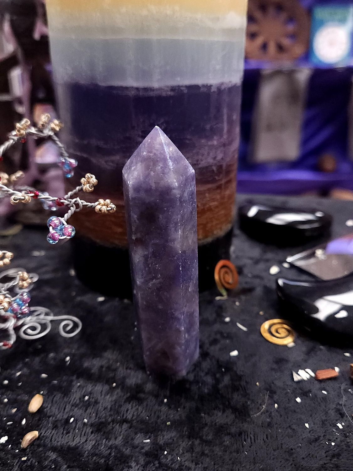 Unicorn Stone Tower 82mm Unicorn stone crystal tower on a black altar cloth in front of a striped purple pillar candle and wire gemstone trees.