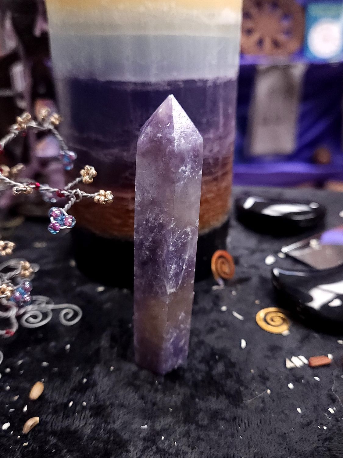 Unicorn Stone Tower 89mm Tall unicorn stone crystal tower on black altar cloth before a layered purple candle, with wire gemstone trees