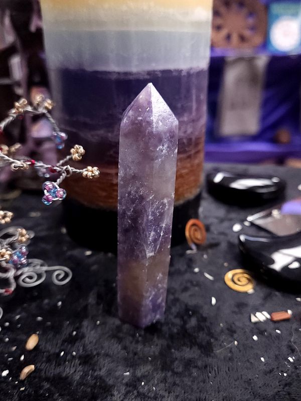 Unicorn Stone Tower 89mm Tall unicorn stone crystal tower on black altar cloth before a layered purple candle, with wire gemstone trees