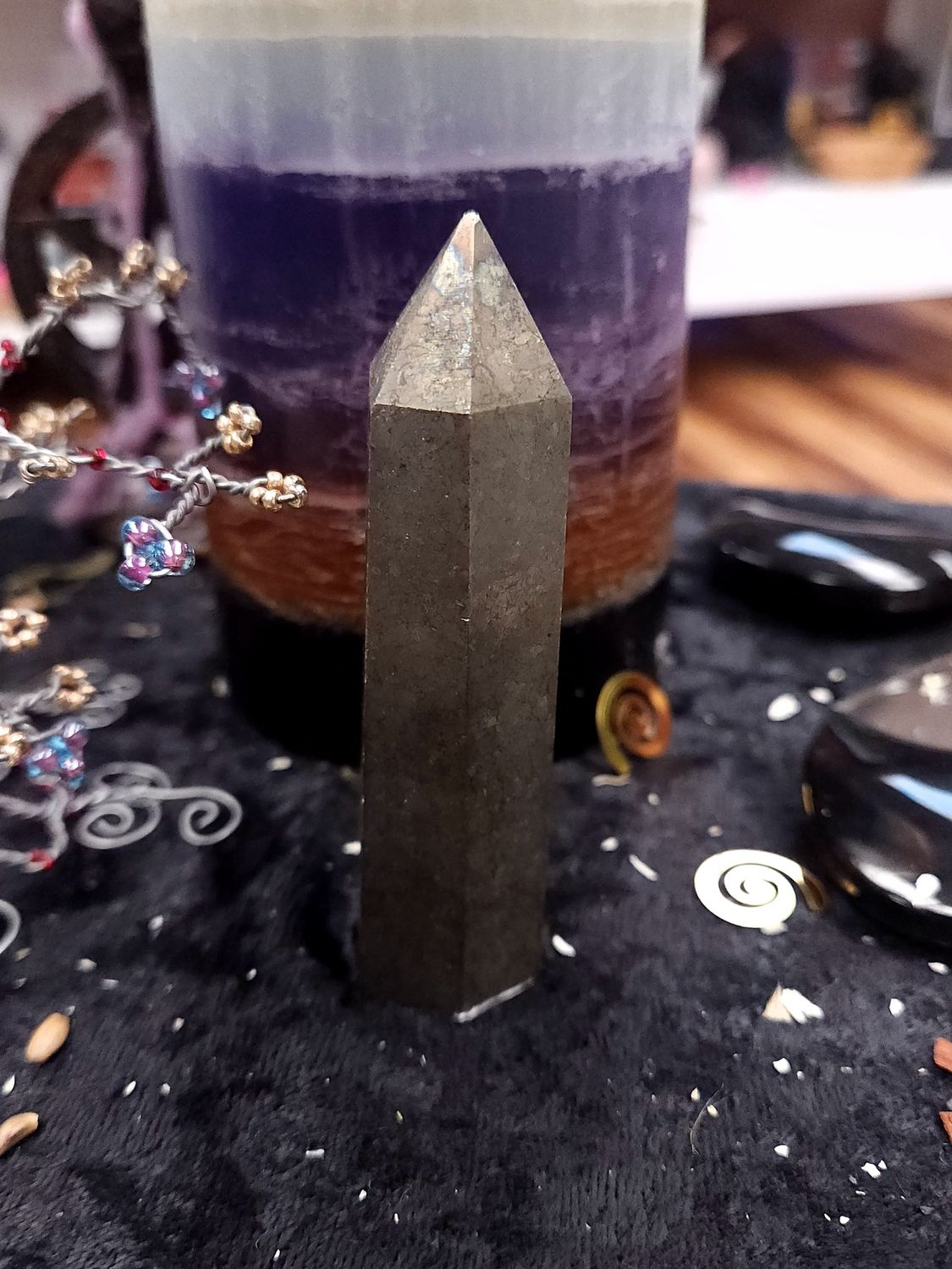 Pyrite Crystal Tower 88mm Metallic pyrite crystal tower on a black altar cloth in front of a layered purple candle with witchy décor in the background.