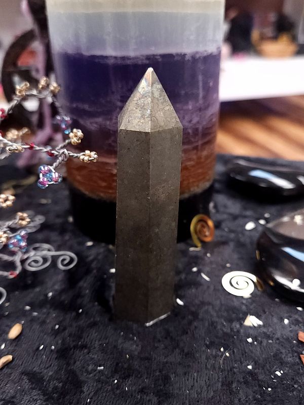 Pyrite Crystal Tower 88mm Metallic pyrite crystal tower on a black altar cloth in front of a layered purple candle with witchy décor in the background.